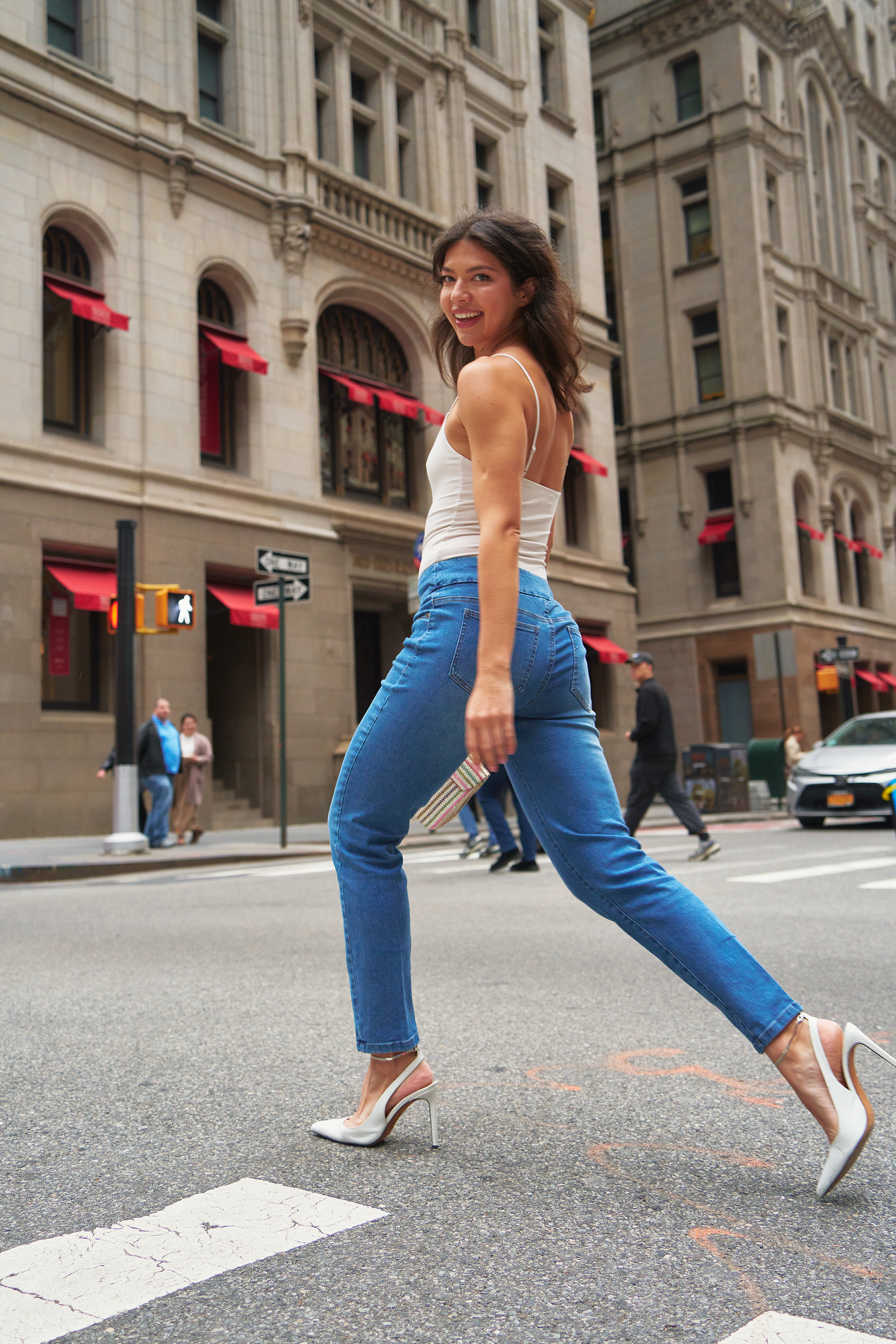 model crossing city street wearing white shirt and tailored light blue pull-on jeans with white high heels