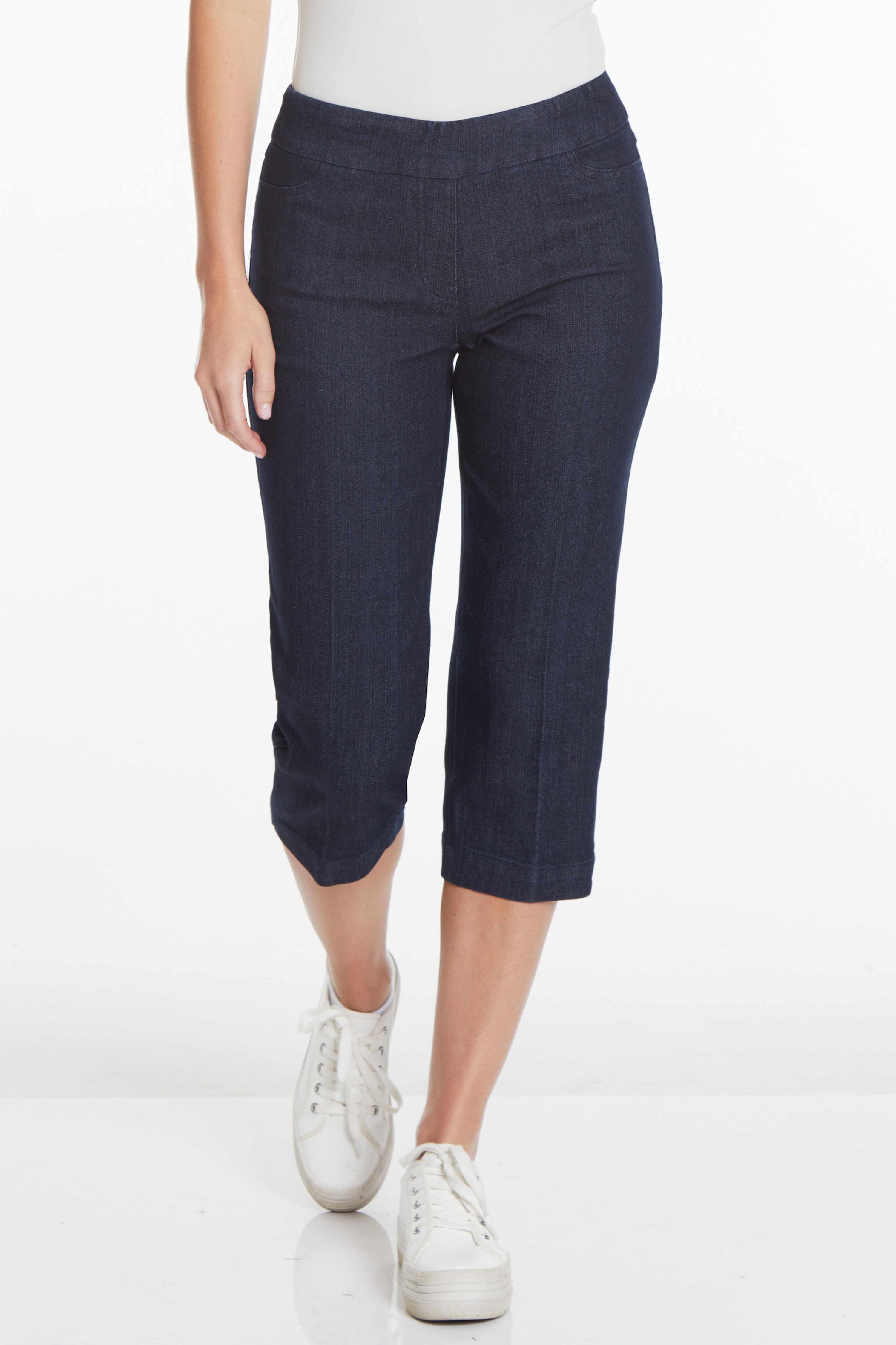 bottom half of model wearing dark wash pull-on denim capris with white tennis shoes
